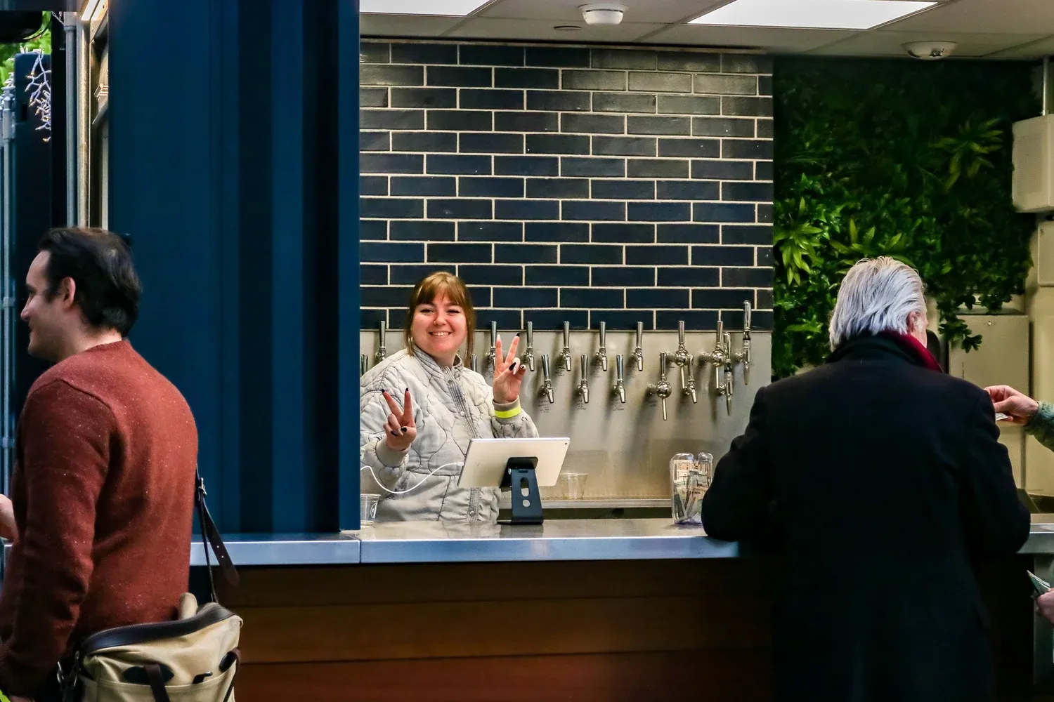 A smiling bartender making peace signs behind the tap wall at the Salesforce Park beer garden.