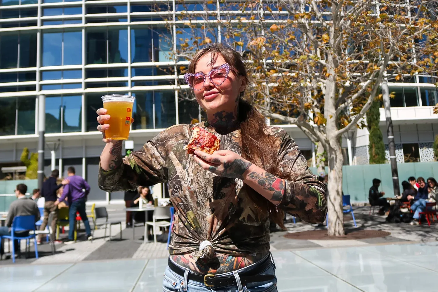 A guest in heart-shaped sunglasses holding a cup of beer and a slice of pizza in Salesforce Park.